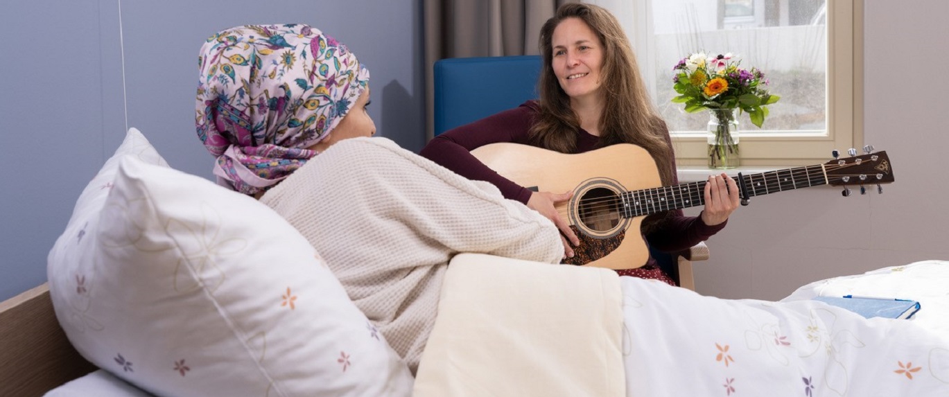 Bild zeigt Gründerin und Liedermacherin Nadine Maria Schmidt mit einer Gitarre in der Hand am Patientenbett